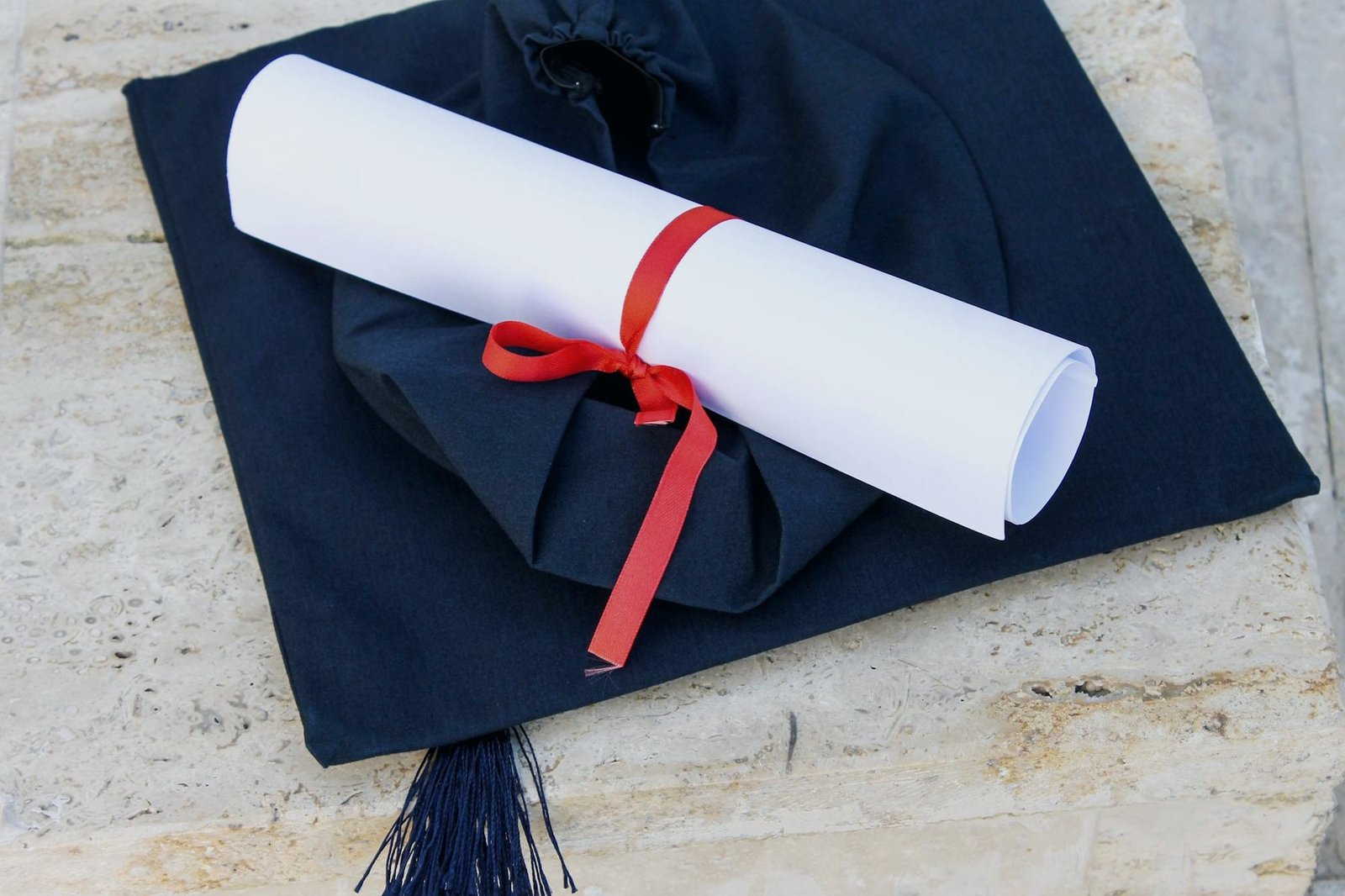 Diploma rolled in red ribbon resting on a navy graduation cap