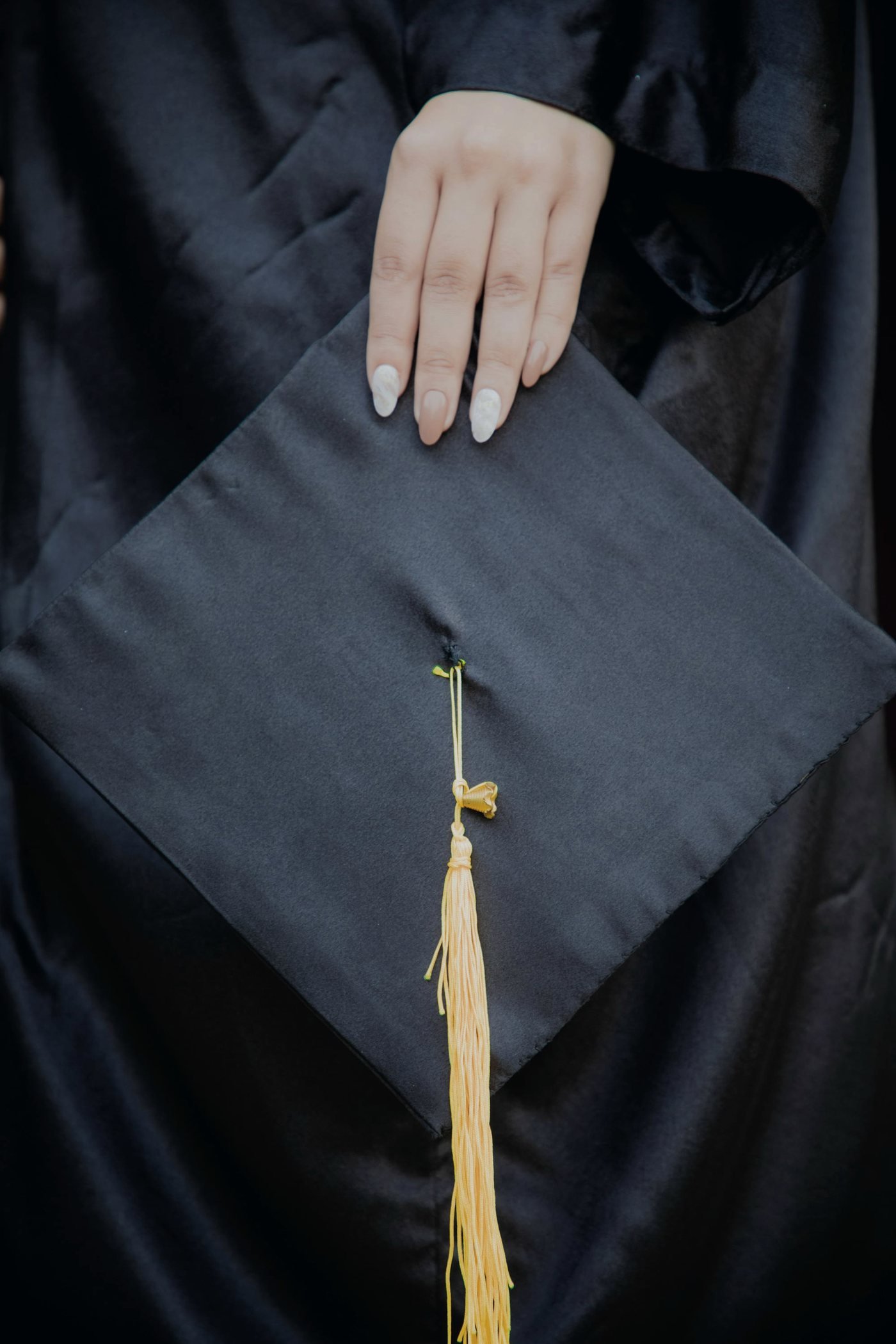 Hand resting on a graduation cap with a gold tassel