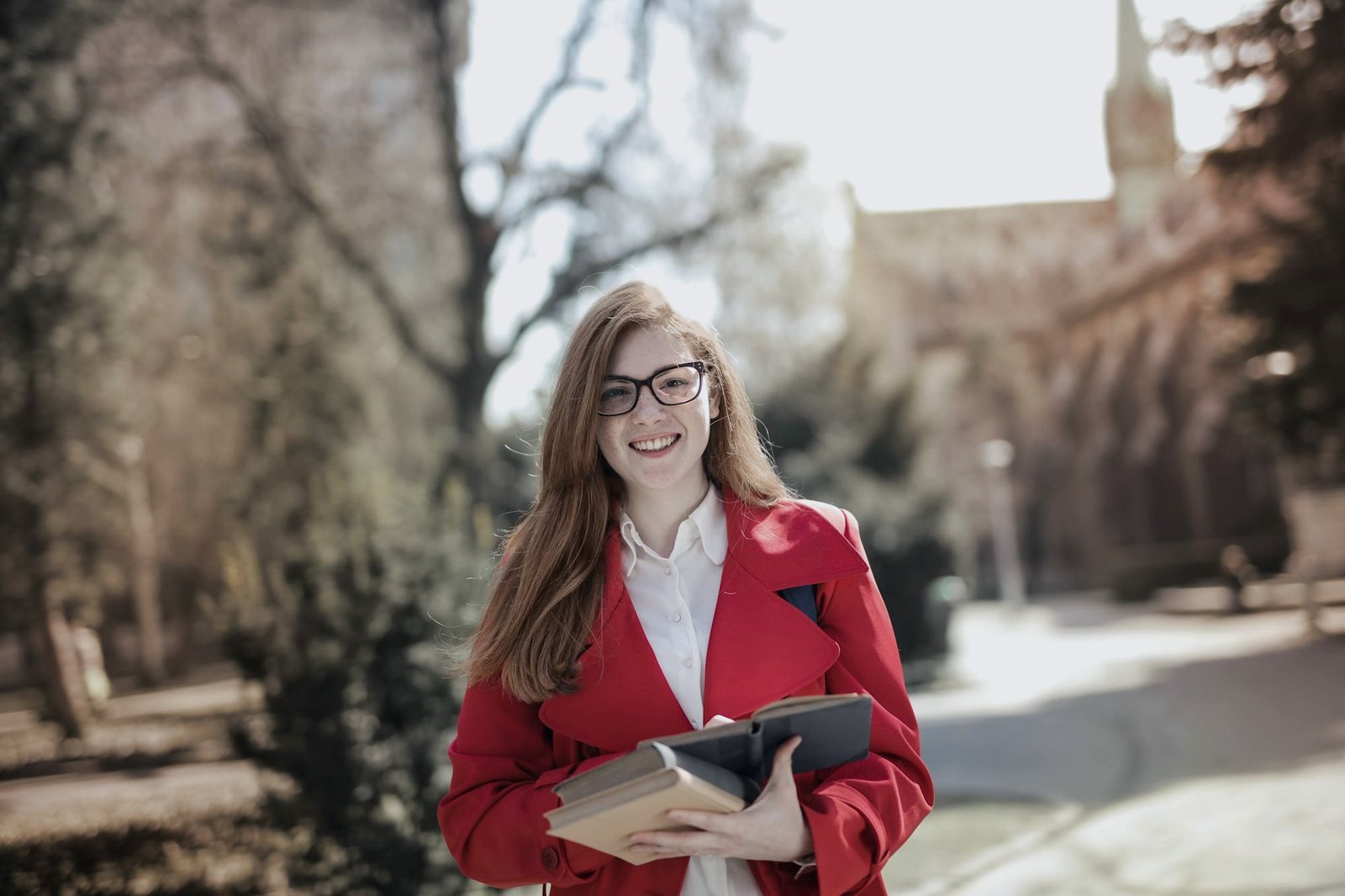 Student in a red coat carrying academic books on a college campus